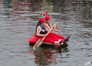 Two women dressed in red pants and red lobster hats paddle a raft on water