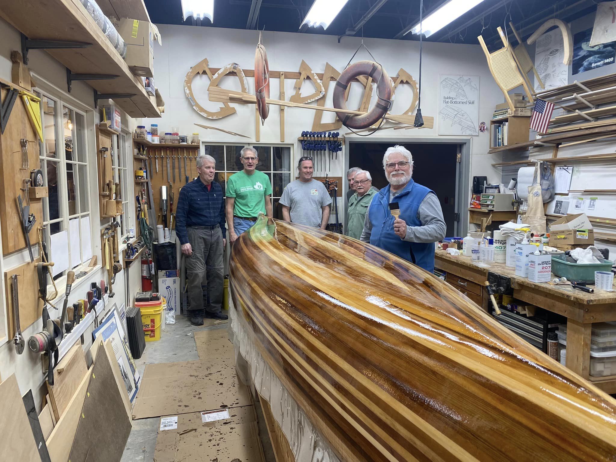 upside down canoe, shiny with first coat of resin. 6 men posing in background of canoe